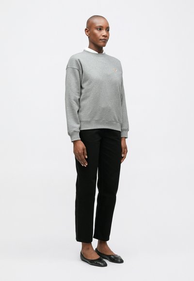 Sudadera gris con cuello redondo, que presenta puños y dobladillo acanalados. Combinada con pantalones negros de corte ajustado y bailarinas negras.