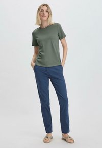 Oliivinvihreä puuvillapaidan, lyhyet hihat, pyöreä pääntie, yhdistetty tummansiniset suorat housut ja beiget sandaalit. Yksinkertainen malli.