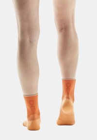 Oranje enkelsokken met verticale ribbelstructuur, een getextureerde voetbed en logodetail op de boord. De stof lijkt elastisch en ademend.
