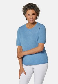 Helles blaues kurzärmliges Pullover mit rundem Halsausschnitt; weiche Textur; kombiniert mit weißen Jeans; zeigt eine lockere Passform und einfaches Design.