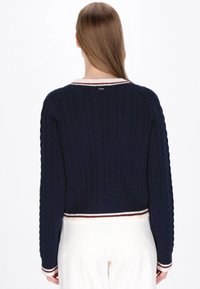 Marineblaue Strickpullover mit rundem Kragen, ausgestattet mit einem weißen und kastanienbraunen gestreiften Saum und einem verkürzten Design. Strukturierter, gemütlicher Stoff.