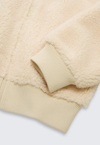 Veste en polaire zippée beige clair avec un extérieur doux et texturé et des poignets côtelés. Dotée d'une fermeture éclair lisse et d'une finition pelucheuse.