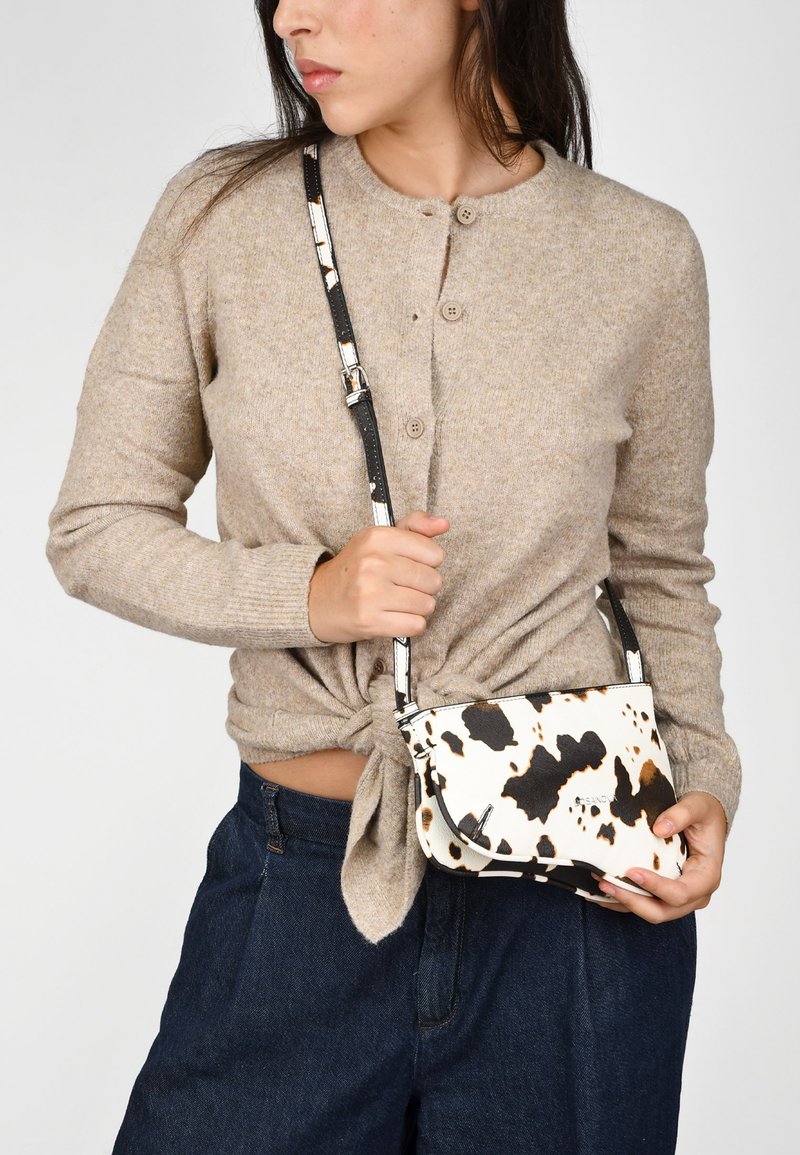 Pequeño bolso cruzado con una base blanca y estampado de vaca en negro y marrón. Tiene un diseño elegante con una correa desmontable y detalles metálicos.