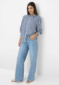 Blauw en wit verticaal gestreepte button-up shirt met lange mouwen, gecombineerd met lichtblauwe wijde jeans en beige sandalen.