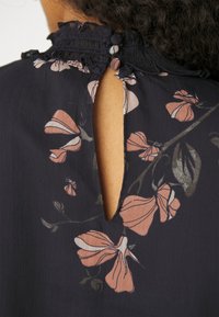 Granatowa blouse w kwiaty z teksturowanym dekoltem, z rozcięciem z tyłu i różowymi wzorami kwiatowymi z zielonymi akcentami. Miękka, lekka tkanina.