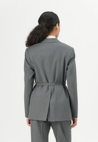 Grå pinstripe blazer med innsvingt midje, med en enkel splitt bak og en klassisk kragedesign.