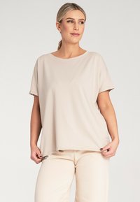 Jasny beżowy top z krótkim rękawem o luźnym kroju, okrągłym dekolcie, miękkiej teksturze i gładkim wykończeniu materiału. W połączeniu z beżowymi spodniami.