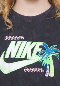 Tmavě šedé tričko s velkým neonově zeleným logem "NIKE", s modrou a zelenou grafikou palmy a růžovými vlnovými akcenty nahoře.