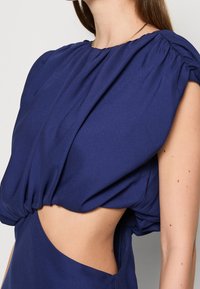 Mörkblå klänning med rund halsringning, puffärmar, sidouttagning och mjukt, flödande tyg med en slät textur.