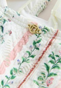 Primo piano di tessuto a motivo floreale con texture goffrata e una piccola fibbia decorativa dorata su tessuto color crema.