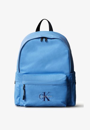 Rucsac Calvin Klein albastru deschis cu fermoare negre, buzunar frontal și mâner negru, pe fundal alb.