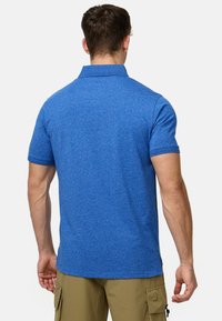 Polo shirt bleu à manches courtes, en tissu texturé, avec un col. Présente des fentes latérales et un contraste sur les ourlets des manches.
