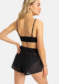 Svart heklet bralette med justerbare stropper, sammen med svarte shorts med et nettmønster og elastisk midje.