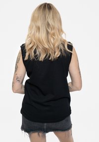 Black sleeveless top made of soft fabric, featuring a relaxed fit. The model has wavy blond hair, visible tattoos on arms, and wears a denim skirt.