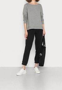 Sudadera gris de manga larga combinada con joggers negros ajustados, zapatillas blancas y un bolso de mano negro con texto blanco. Diseño plano y casual.