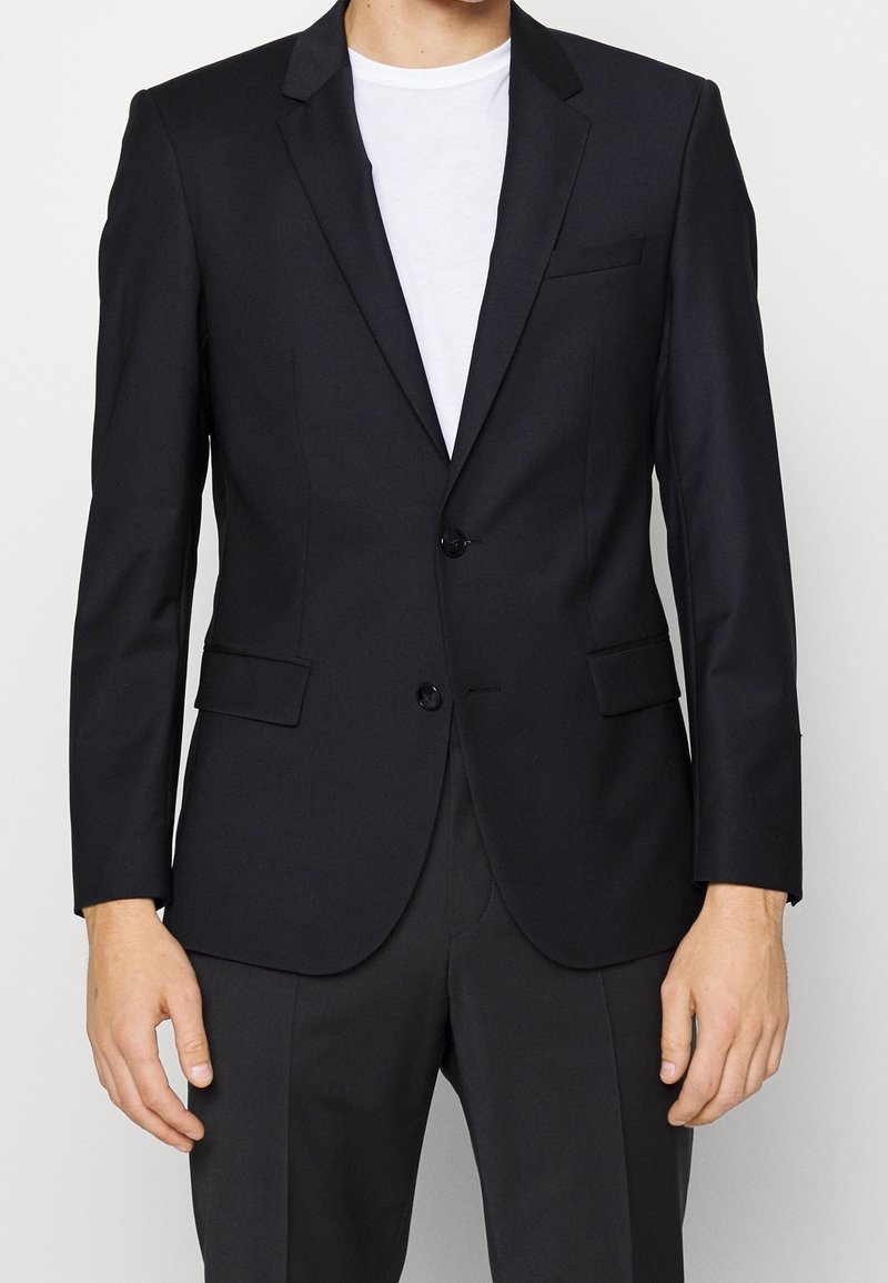 Blazer nero realizzato in tessuto liscio; presenta una chiusura a due bottoni, revers a punta e tasche laterali; abbinato a una t-shirt bianca.