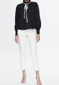 Zwarte katoenen blouse met een rimpelachtige halslijn en een witte strik, gecombineerd met witte strakke trousers met zijsplitten aan de zoom.