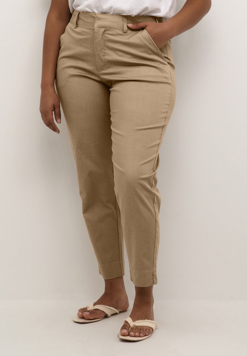 Beige, skræddersyede bukser med slim fit, der har sidelommer, en glat struktur og oprullede manchetter, parret med simple, lyse sandaler.