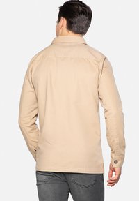 Beige jakke lavet af bomuld, med en knappet manchet og detaljer på ryggen. Designet inkluderer lange ærmer og en lige pasform.