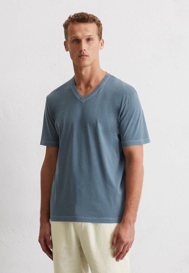 T-shirt à col en V, à manches courtes, en coton bleu délavé et doux. Design simple avec une coupe décontractée et un minimum de détails de couture à l'ourlet.