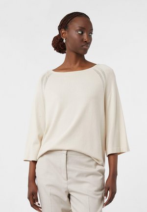 Blusa beige chiaro con scollatura ampia e maniche a 3/4. Presenta dettagli a maglia testurizzata nelle cuciture raglan. Tessuto morbido e liscio.