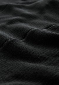 Tejido de punto negro con una superficie suave y texturizada. El material presenta sutiles estrías y variaciones, lo que realza su profundidad visual.