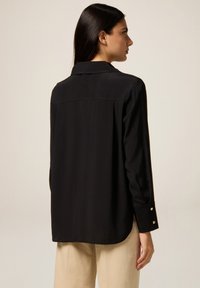 Black long-sleeve blouse with a collar, smooth fabric, and buttoned cuffs. Features a back yoke design for an elegant silhouette.
