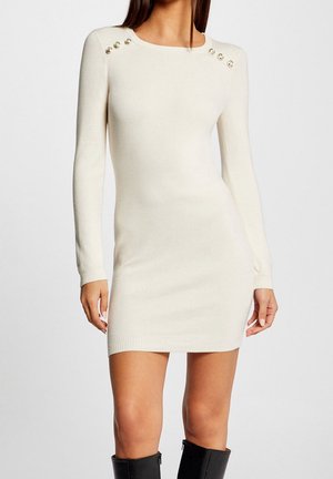 Gebreide crème jurk met lange mouwen en een ronde halslijn, voorzien van vijf metalen knopen op elke schouder en geribbelde zoom en manchetten.