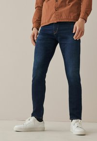 Donkerblauwe denim jeans met een slim fit, met subtiele vervagingdetails. G gedragen met witte sneakers voor een casual look.