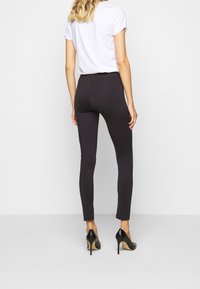 Svarta leggings i elastiskt material, åtsittande design, slät textur, kombinerat med svarta högklackade skor och en vit t-shirt med kort ärm.