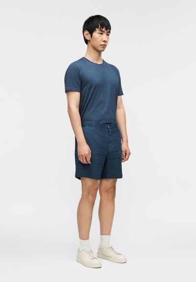 Μπλε κοντομάνικο μπλουζάκι συνδυασμένο με σκούρο μπλε σορτς. Τα αθλητικά παπούτσια είναι μπεζ, με ανοιχτόχρωμες κάλτσες. Απλός, καθημερινός στυλ με άνετη εφαρμογή.