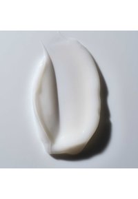 Trace lisse et courbée de crème blanche ou de lotion sur une surface claire avec une ombre subtile sur le côté droit.