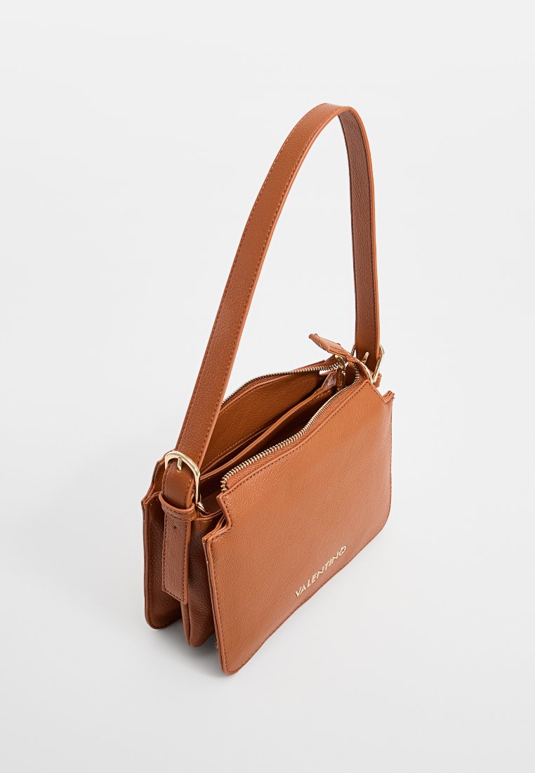 Sac à main en cuir marron avec une bandoulière amovible, doté d'un compartiment zippé et d'un détail de logo en doré. Forme rectangulaire compacte.