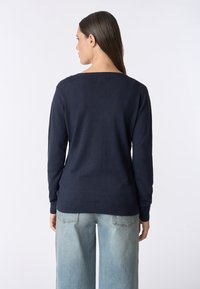 Maglione blu navy con una vestibilità rilassata, scollatura rotonda e maniche lunghe. Realizzato in un materiale morbido, mostrato di schiena con jeans chiari.