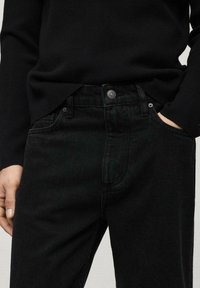 Jeans de mezclilla negra de corte ajustado, con un bolsillo frontal y detalle de botón de metal en la cintura. La tela tiene una textura sutil.