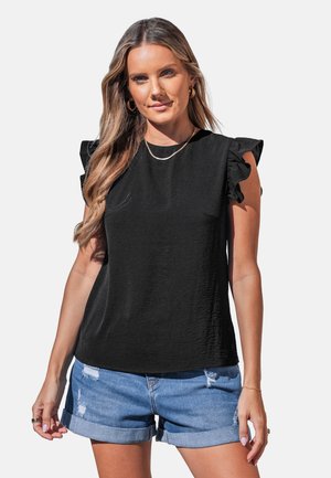 Mujer con un top negro sin mangas con volantes, combinado con shorts vaqueros azules claros, enrollados y desgastados, pendientes de aro dorados y un collar.