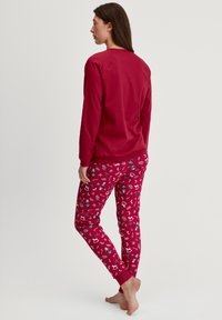 Rode longsleeve top met geribde manchetten, gecombineerd met rode pyjamabroek met patronen en kleurrijke illustraties, voorzien van een elastische tailleband.
