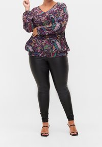 Top multicolore con motivo paisley, maniche lunghe e scollatura a V. Abbinato a leggings neri attillati e sandali neri con cinturini.