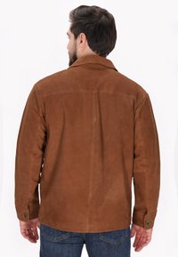 Brun ruskindjakke med klassisk krave, knaplåste ærmer og et simpelt bagsysmønster. Båret over blå jeans.