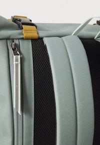 Zaino blu chiaro con dettagli in rete nera, dotato di tasca con zip e spallacci gialli regolabili, progettato per praticità e durata.