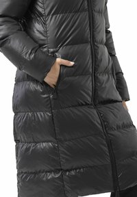 Schwarzer Steppmantel mit glänzendem Finish, bestehend aus horizontalen gesteppte Abschnitte, zwei seitlichen Reißverschlusstaschen und einem zentralen Frontreißverschluss.