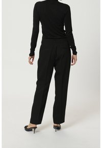 Czarne, dopasowane spodnie o prostym kroju, wykonane z gładkiej tkaniny. Posiadają dwie tylne kieszenie i są zestawione z czarną bluzką z długim rękawem oraz szpilkami.