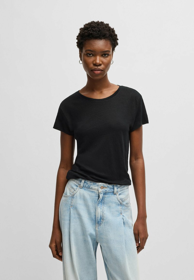 T-shirt nero a maniche corte con scollo rotondo e morbida texture, abbinato a jeans high-waisted azzurri con dettagli frontali plissettati.