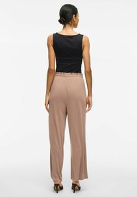 Top negro sin mangas combinado con pantalones de pierna ancha beige que tienen aberturas laterales en el dobladillo y una cinturilla elástica. Zapatos de tacón completan el conjunto.