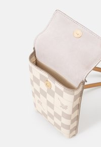 Béžová kostkovaná taška s měkkým semišovým klopou, zlatým zapínáním na druk a hladou vnitřní podšívkou. Na vnější straně jsou jemné květinové vzory.