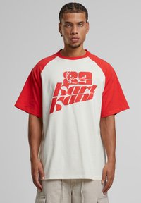 Red and white oversized T-shirt with raglan sleeves, featuring bold red graphic text on front. Made from soft cotton fabric.