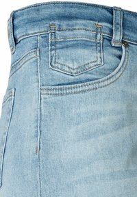Jeans de mezclilla azul claro que muestran el bolsillo superior, el lazo del cinturón y las costuras naranjas detalladas en la textura de la tela.