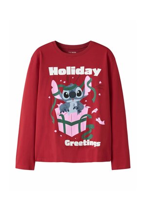 Czerwona koszulka z długim rękawem z postacią z kreskówki wychodzącą z różowego pudełka na prezent oraz słowami "Holiday Greetings" białymi literami.