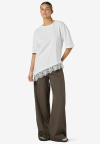 Hvit oversized t-skjorte med buet kant og blondekant. Kombinert med løse brune bukser og svarte joggesko.