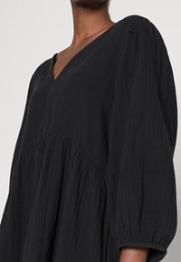 Svart, medellång klänning i texturerad tyg, med V-ringning, puffärmar och en flytande silhuett med rynkdetaljer.